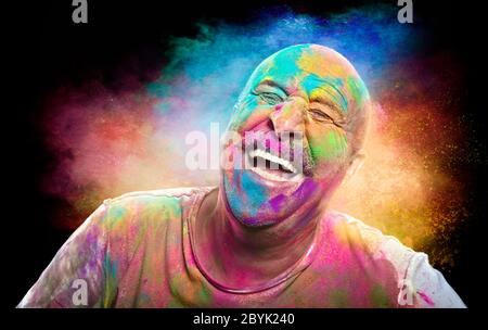 Portrait of bald cheerful man with colored face celebrating holi color festival. Man having fun with colorful powder. Stock Photo