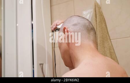 A man shaves his head in front of a mirror in the bathroom by hair clippers. copy space. closeup. Stock Photo