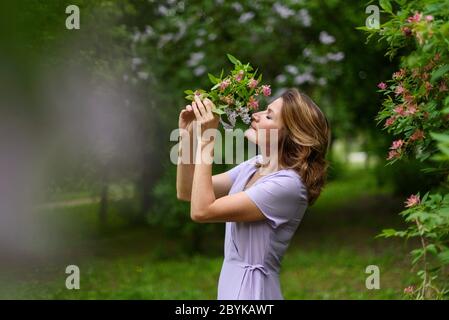 Woman in lilac dress sniffs bouquet of flowers with closed eyes and ...