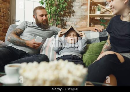 Happy family at home spending time together. Having fun, look cheerful and lovely. Mother, father and son reading book during remote school studying. Parents helping. Childhood, domestic life concept. Stock Photo