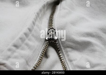 Macro close up of isolated white casual denim jeans pants with metal teeth zipper (focus on slider) Stock Photo