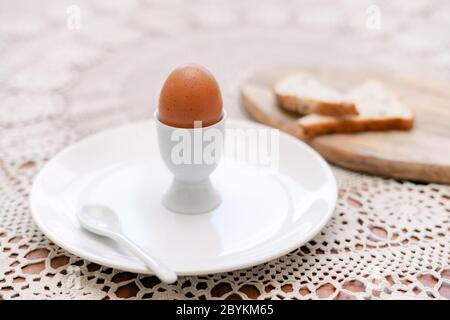 Tasty boiled egg in a cup with crunchy toasted bread for breakfast. Healthy meal on the kitchen table. Stock Photo