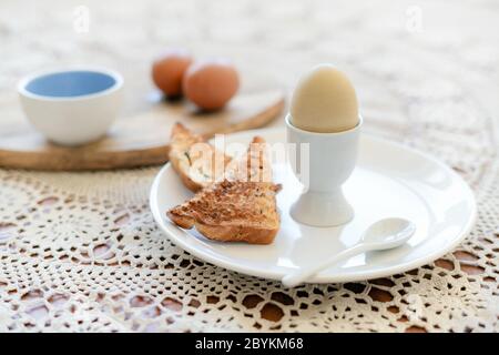 Tasty boiled egg in a cup with crunchy toasted bread for breakfast. Healthy meal on the kitchen table. Stock Photo