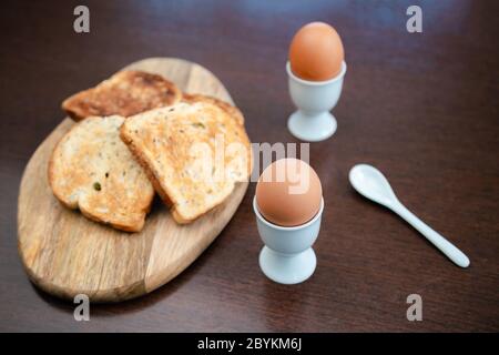 Tasty boiled egg in a cup with crunchy toasted bread for breakfast. Healthy meal on the kitchen table. Stock Photo