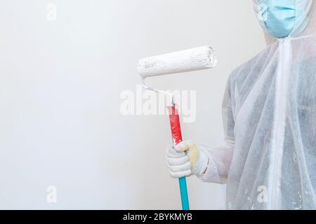 Man in protective work clothes painting the walls white colour with a paint roller. Home renovation project. Apartment renewal concept. Stock Photo