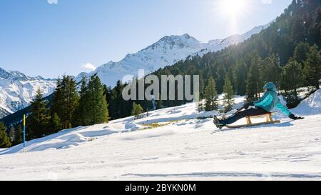 Speeding downhill on wooden sled. Happy influencer having fun with wood vintage sledding on snow high mountains - Natural sled runs Stock Photo