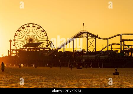 'Santa Monica' pier with ferris wheel and roller coaster silhouetted against the golden setting sun. California, United States of America. Oct 2019 Stock Photo