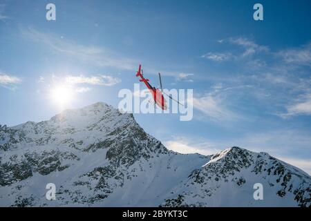 Red rescue helicopter flying over the view of the snowy rocks in Alpine ski resort Zermatt near Matterhorn mountain. Winter nature landscape of Swiss Stock Photo