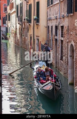 Couple on a gondola trip on the Rio de San Salvador canal in Venice, Italy while the gondolier is distracted using his mobile phone Stock Photo