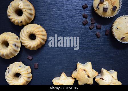 Several small cakes or muffins lie on a slate black board and form a frame Stock Photo