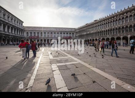 People enjoying the late afternoon sunshine amongst the pigeons on St Mark's Square in Venice, Italy showing the surrounding architecture Stock Photo