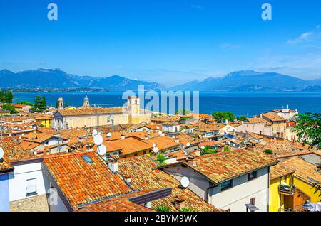Aerial panoramic view of Desenzano del Garda town with bell tower of Duomo di Santa Maria Maddalena Cathedral church, red tiled roof buildings, Garda Lake, mountain range, Lombardy, Northern Italy Stock Photo