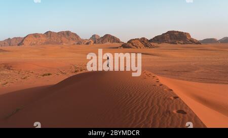 Crazy man running overlooking the red sand desert as seen with a cloudy golden sunset in Wadi Rum, Jordan. Fearless hiker he lost in the desert. Stock Photo