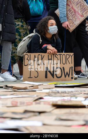 A girl squats beside protest signs laid out in front of the Palace of Westminster, Black Lives Matters protest, Parliament Square, London, 7 June 2020 Stock Photo