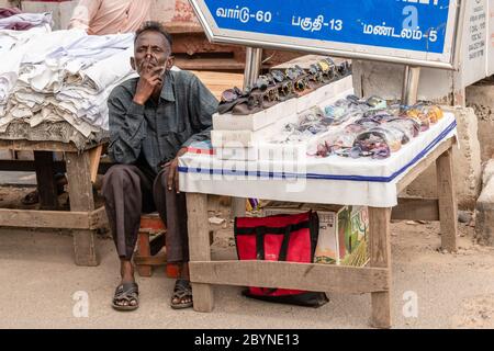 Chennai, Tamil Nadu, India - August 2018: An Indian street vendor selling sunglasses sitting beside his pavement shop with a curious expression on his Stock Photo