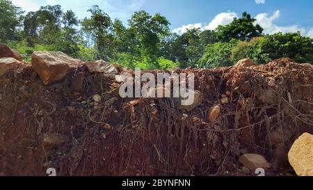 damage road cut of soil layer with different visible underground to water erosion as the cliff Stock Photo