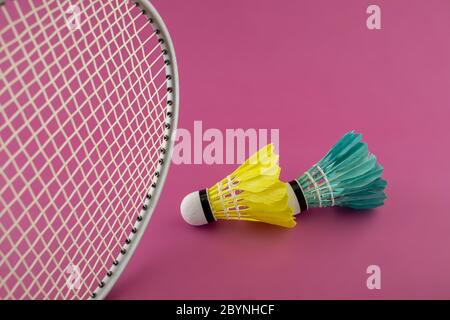 Badminton rackets and colorful feathered shuttlecocks in green and yellow on a pink background Stock Photo