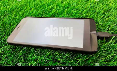 mobile phone charging isolated on green grass background Stock Photo