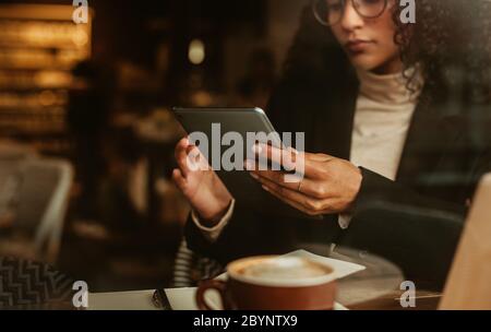 Woman sitting at a coffee shop and working on her digital tablet. Businesswoman using tablet computer while sitting at a cafe. Stock Photo