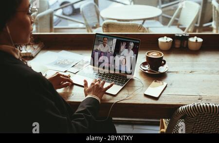 Businesswoman making a video call at a cafe. Woman sitting at a coffee shop having a video conference with her team. Stock Photo