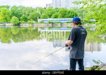 Manhattan, New York - May 30, 2020: Fisherman Casts His Line off the Inwood Hill Park Shores. Stock Photo