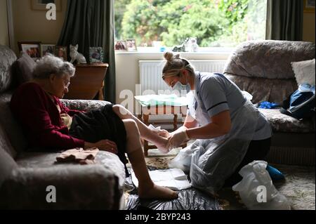 District nurse Rebecca McKenzie (right), wearing personal protective equipment (PPE) changes the dressings on the legs of 86-year-old Margaret Ashton (left) to treat her leg ulcers during a home visit in Grimsby, Lincolnshire. Stock Photo