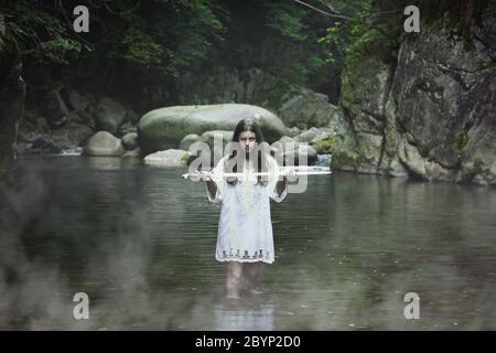 Beautiful dark girl with a sword in a mountain stream. Fantasy and halloween concept Stock Photo