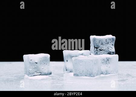 several melted ice cubes with drops on a dark black background Stock Photo