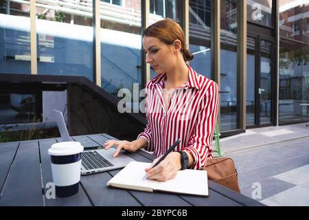 Caucasian woman working on a computer and taking notes in a sunny day Stock Photo
