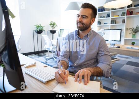 Caucasian man working on computer ans taking notes in an office Stock Photo