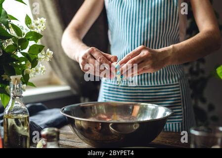 A woman is breaking an egg to make dough. The process of making handmade pasta in a pleasant and cozy home environment. Stock Photo