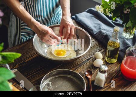 A woman is breaking an egg to make dough. The process of making handmade pasta in a pleasant and cozy home environment. Stock Photo