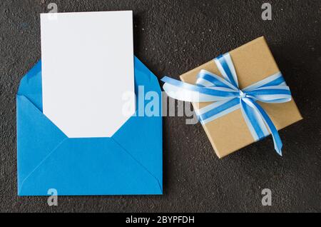 Blue envelope with blank white paper and present or gift box. Greeting card for Father's or Grandfather's Day. Mockup of letter. Top view with space f Stock Photo