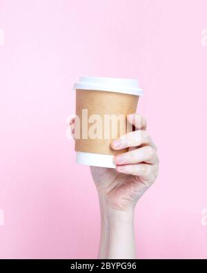 Woman's hand holds paper cup with coffee on pink background Stock Photo