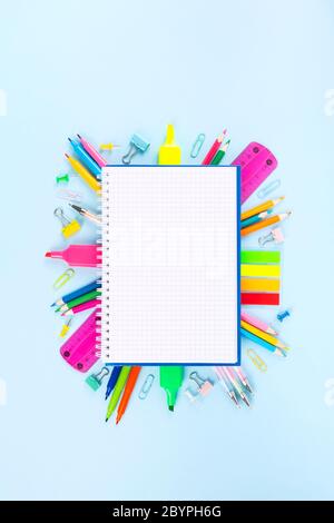 Checked notebook surrounded by various school office and painting supplies on blue background. Back to school concept. Top view. Copy space Stock Photo