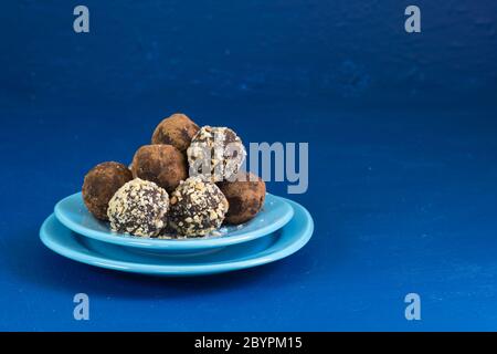 Several homemade chocolate energy balls made of dried fruits, nuts and cocoa, lie in a plate on a blue background. Healthy lifestyle Stock Photo