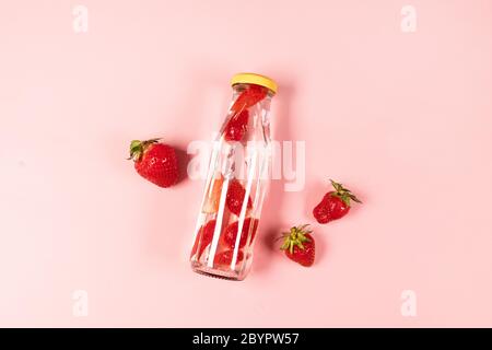 Bottle of detox water, cocktail, lemonade or tea with fresh strawberry summer fruit on pnk background. Summer composition, minimal style Stock Photo