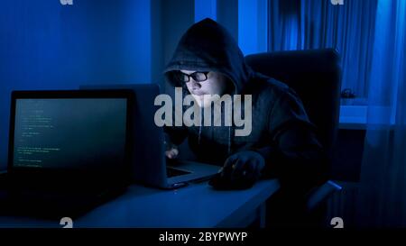 Male hacker working on laptop from home at night Stock Photo