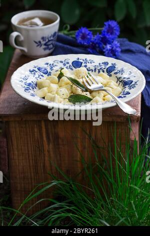 Breakfast of lazy dumplings with sage and chamomile tea on a wooden stool in the garden. Stock Photo