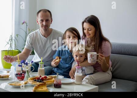 Happy family, having pancakes for breakfast, eating in living room, talking and laughing, cozy home Stock Photo