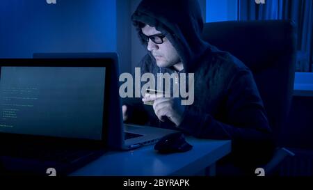 Male hacker in hood stealing money from credit card at night Stock Photo