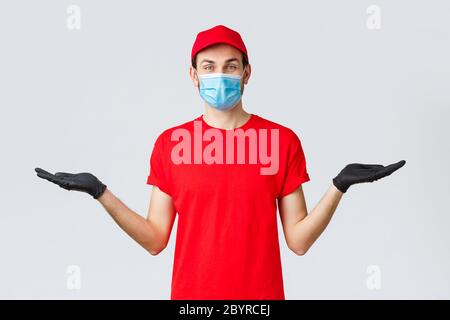 Groceries and packages delivery, covid-19, quarantine and shopping concept. Friendly delivery man in red uniform, face mask and gloves, holding two Stock Photo