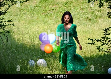 Beautiful woman in green dress in nature with balloons Stock Photo