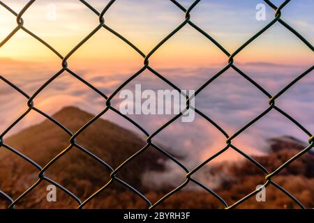 Sunrise light over the sea of clouds through the fence (closeup focus on the fence) Stock Photo