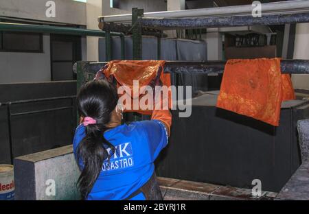 Worker hang wet Batik to dry in Winotosastro factory in Yogyakarta, Java, Indonesia. Batik motif sample designs on cloth. Hand drawing the white fabri Stock Photo