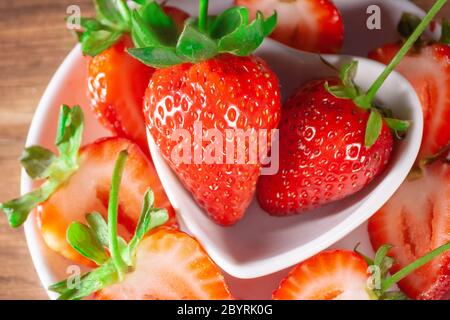 large fresh red strawberries with green stem on white ceramic plates with many strawberries around in a close view Stock Photo