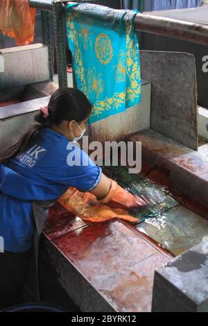 Worker washes dyed Batik to dry in Winotosastro factory in Yogyakarta, Java, Indonesia. Batik motif sample designs on cloth. Hand drawing the white fa Stock Photo