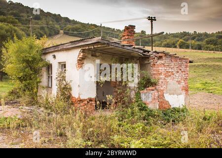 Small Abandoned Derelict Brick House Overgrown by Vegetation in Countryside Stock Photo