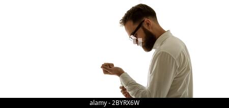 Closeup portrait from the side of handsome man in studio. Model fastens button on his sleeve of white shirt isolated on white background. Morning rout Stock Photo