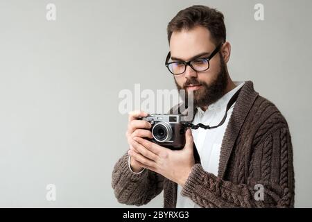 Confident hipster photographer with camera on a strap posing isolated on white background. Model wearing warm brown sweater and has a beautiful black Stock Photo